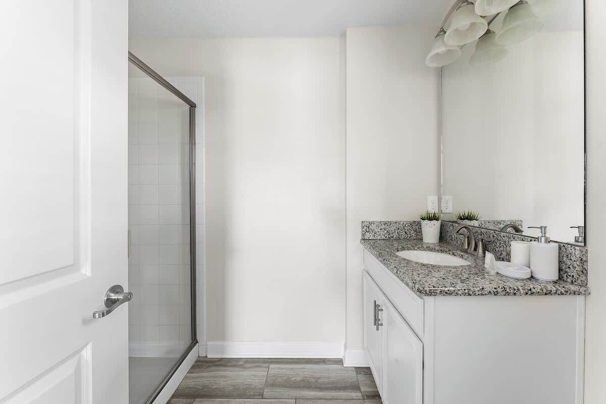 Un bagno con box doccia in vetro, pareti bianche, un piano di lavoro in granito e uno specchio.