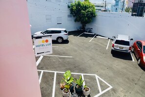 Un estacionamiento de hotel con espacios delimitados, un cartel que dice 'HOTEL LUZ' y plantas en macetas.