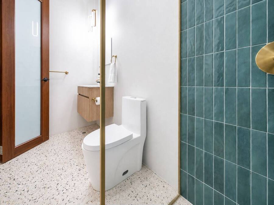 Un baño con inodoro, un armario de madera y una pared con azulejos color turquesa.