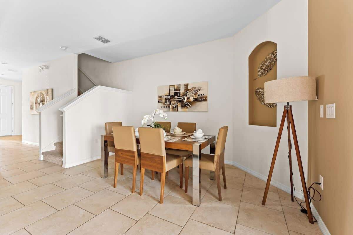 A dining area with a wooden table and chairs, a painting on the wall, and a floor lamp.