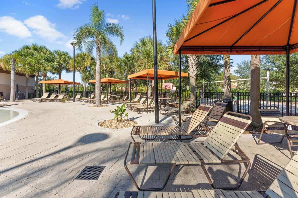 A poolside area with sun loungers and umbrellas, surrounded by palm trees.