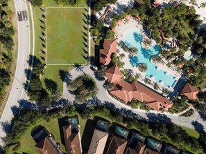 An aerial view of a resort with a swimming pool, palm trees, and a road. - Themed Mickey Bedroom 4BR at Solterra (Davenport)