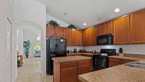 Una cocina con armarios de madera, encimeras de granito, un refrigerador negro, un microondas y una estufa.