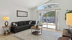 Una sala de estar moderna con un sofá modular, una mesa de centro redonda, una lámpara y un amplio ventanal con cortinas.