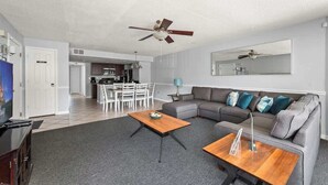 Un salon moderne avec un canapé gris, une table basse en bois et un ventilateur de plafond.