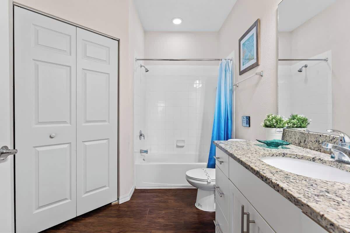 Een badkamer met een wit toilet, een badkuip en een douche. Er is een wastafel met een granieten aanrechtblad en een spiegel erboven.