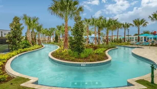 A pool with a curved design, surrounded by palm trees and a clear blue sky. - Pet Friendly Amazing 5 BR sleeps 10 (Kissimmee)