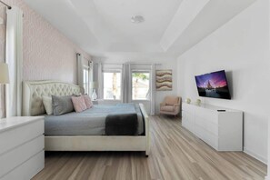 Um quarto com uma cama, televisão, poltrona e cômoda.