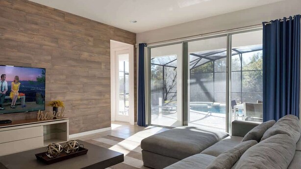 A modern living room with a large grey sofa, a flat-screen TV, and a wooden wall.