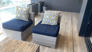 Two wicker lounge chairs with cushions, a small wooden table, and a view of the outdoors.