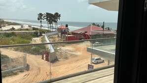 A view from a window overlooking a beach area with a dirt path, palm trees, and a red-roofed building.