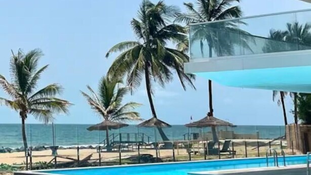 A pool area with clear blue water, palm trees, and a view of the ocean.