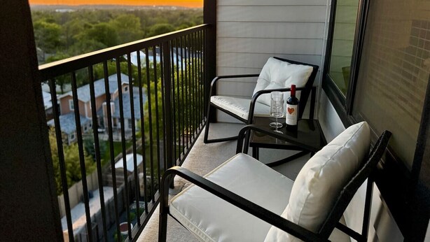 A balcony with two chairs and a table, overlooking a residential area during sunset. - New Modern 1BD/1BA~Pet Love Loft (Austin)