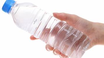 Eine klare Plastikwasserflasche mit blauem Verschluss, gehalten von einer Hand.