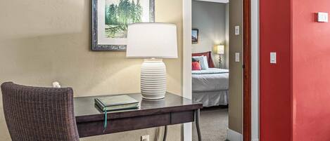 Una habitación de hotel con escritorio, silla, lámpara y cama con almohadas y manta.