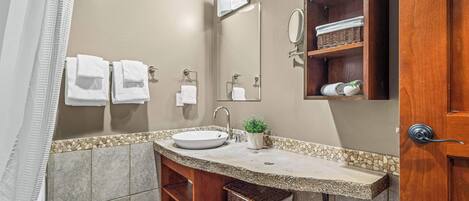 Une salle de bain équipée d’un lavabo, d’un miroir, d’un porte-serviettes et d’une petite plante en pot.