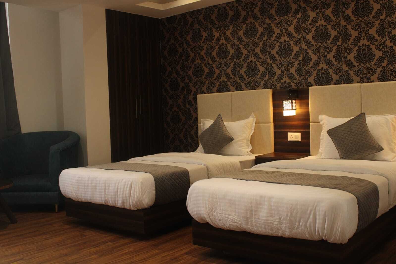 A hotel room with two beds, dark curtains, patterned wallpaper, and a wooden floor.