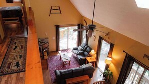 Un loft spacieux avec un plafond haut, un coin repas avec une table et des chaises en bois, un canapé et une grande fenêtre laissant entrer la lumière naturelle.