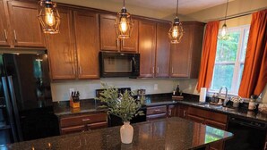Une cuisine moderne avec des meubles de couleur bois foncé, un grand îlot central doté de tabourets, un réfrigérateur en acier inoxydable et des luminaires suspendus.