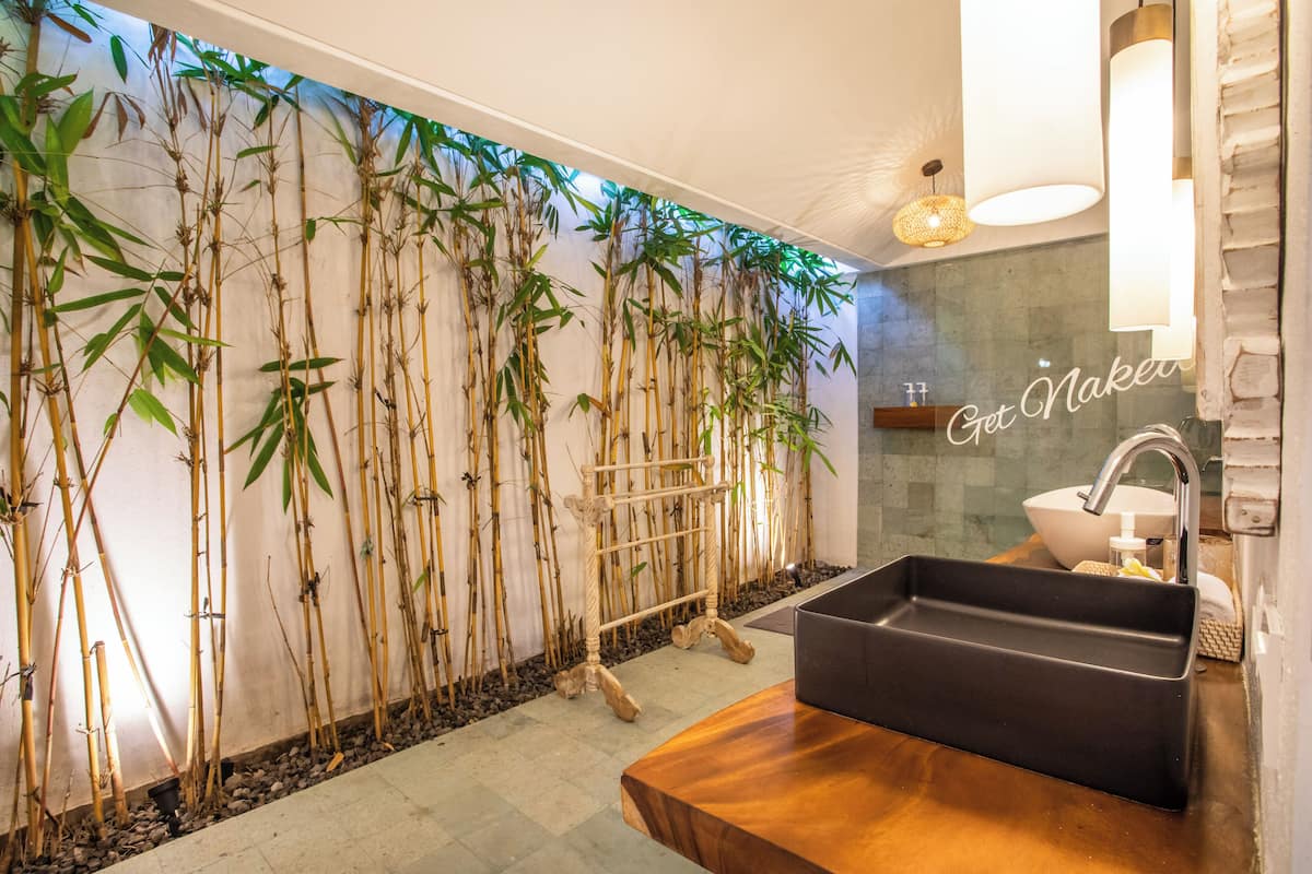 A bathroom with a bamboo wall, a wooden vanity, and a black sink.