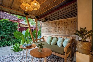 Un rincón exterior acogedor con un banco de madera, una mesa redonda y una planta en maceta.