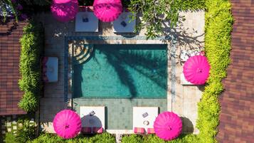 Vista aérea de una piscina rectangular rodeada de vegetación exuberante y sombrillas rosas.