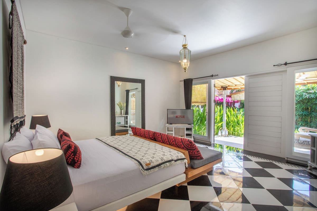 A modern bedroom with a bed, bedside lamps, a TV, and a view of a garden through a sliding door.