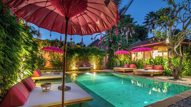 Un espace piscine agrémenté de chaises longues et de parasols, le tout entouré d’une végétation luxuriante.