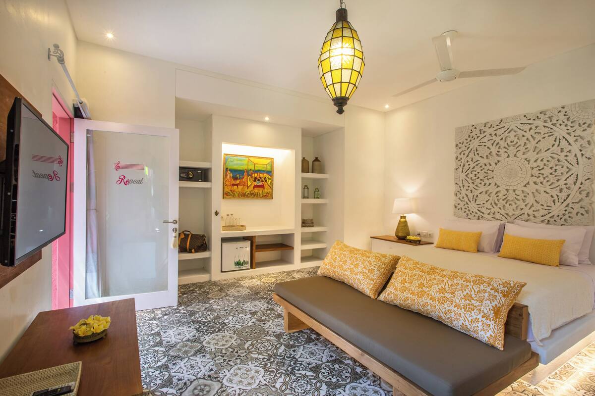 A modern hotel room with a bed, a bench, a TV, and a decorative wall.