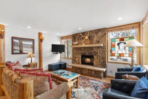 Uma sala de estar acolhedora com lareira de pedra, assentos confortáveis e uma grande janela com vista.