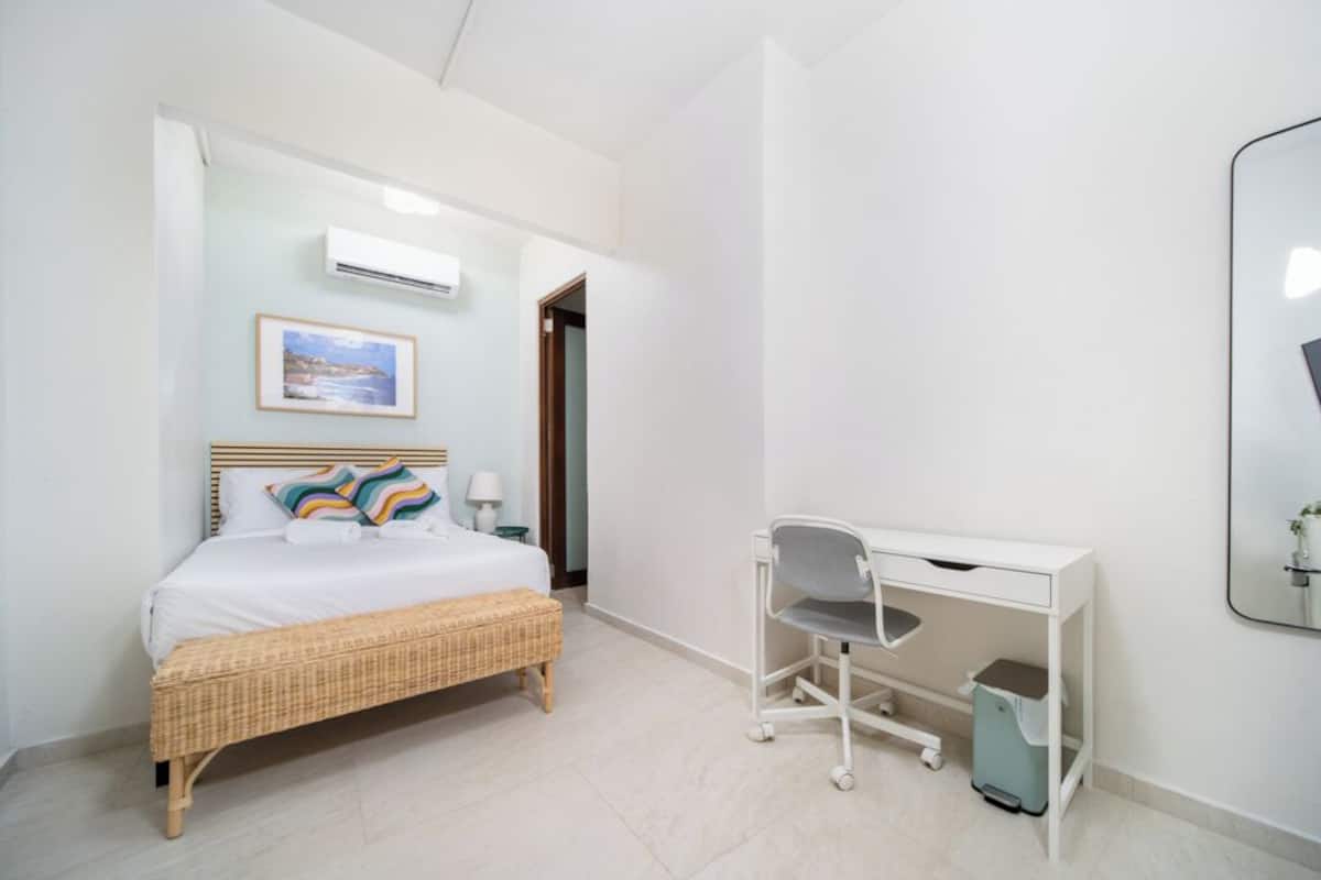 Une chambre d’hôtel comprenant un lit, une table de chevet, une chaise, un bureau et une poubelle.