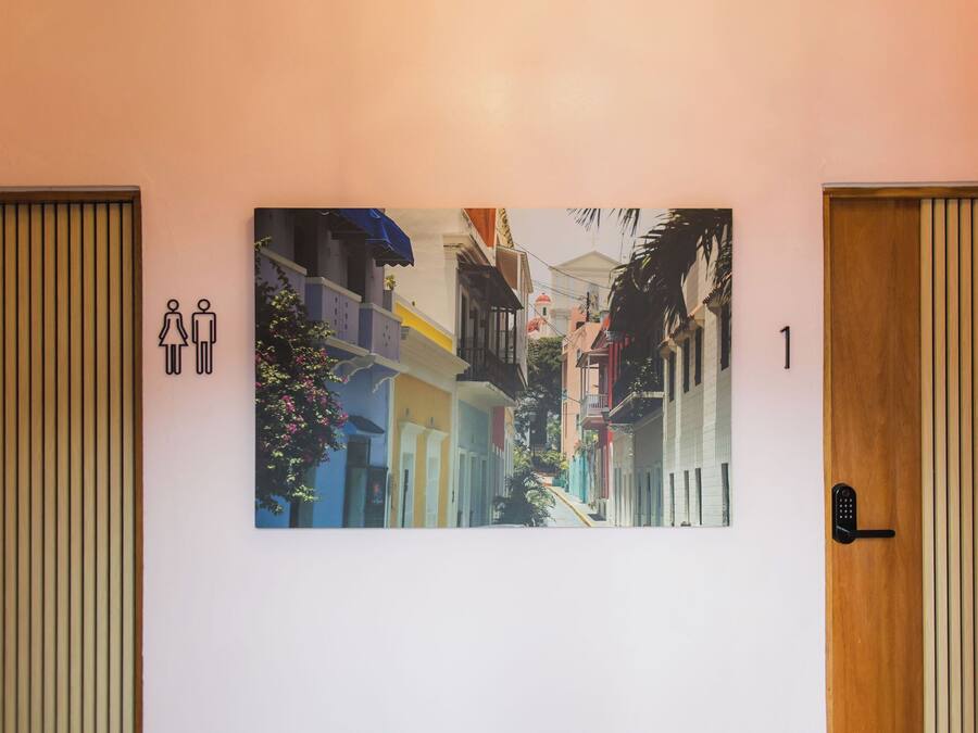 A hallway with a large painting of colorful buildings, a door with a keypad lock, and a toilet sign.