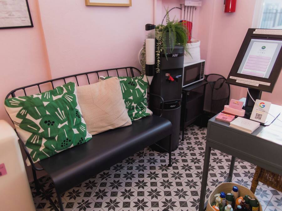 A room with a black metal bench, green patterned pillows, a small desk with a computer, and a tiled floor.
