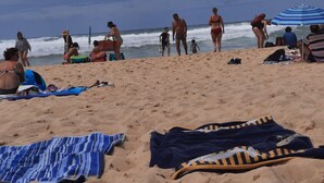 Una playa arenosa con gente, algunos de pie y otros sentados, y algunos sombrillas.