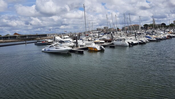 Una marina con numerosos barcos amarrados, una superficie de agua tranquila y un cielo nublado.