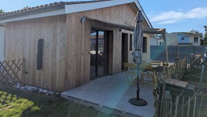 Una construcción de madera con techo de tejas, una puerta y un patio con mesa y sillas.