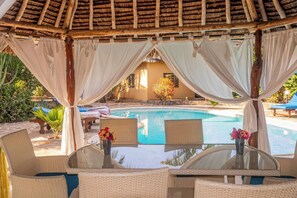 A covered outdoor seating area with wicker chairs and a glass table, overlooking a pool. - Private Villa Watamu (Watamu)