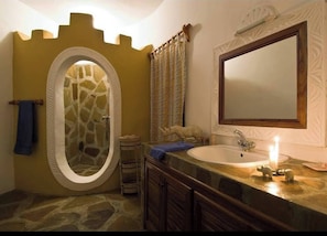 A bathroom with a stone shower enclosure, a large mirror, and a sink with a candle. - Private Villa Watamu (Watamu)