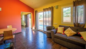 A spacious living area with a sofa, a dining table, and a view of a pool through large windows. - Club Villamar - Charming house with pool in the Rio de Oro urbanisation – Calonge (Calonge)