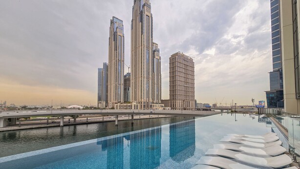 Een modern hotel met een zwembad, hoge gebouwen op de achtergrond en een heldere lucht.