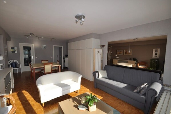 A living room with a sofa, a dining table with chairs, a kitchen area, and a bathroom visible through an open door. - Studio in Knokke-heist Near the Beach (Knokke-Heist)