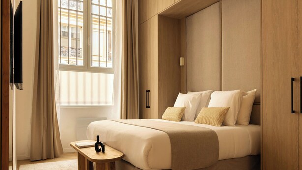 A neatly arranged hotel room with a large bed, a bedside table, and a window with curtains. - Sublime Air-conditioned Flat Le Marais (Paris)