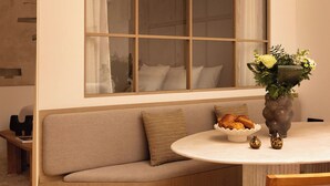 A modern dining area with a round table, a wooden chair, a beige sofa, and a large window with curtains. - Sublime Air-conditioned Flat Le Marais (Paris)