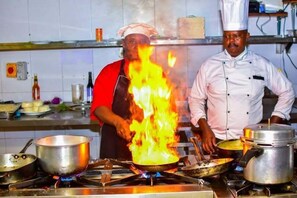 A kitchen with chefs cooking, pots on the stove, and a tiled backsplash. - Breeze Hotel Nyahururu (Nyahururu)