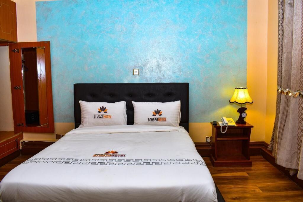 A hotel room with a bed, a nightstand with a lamp, and a door.