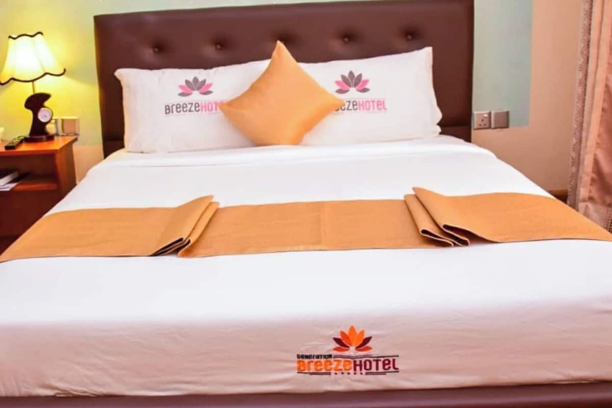 A neatly made hotel bed with white bedding, two pillows, and a brown throw blanket.
