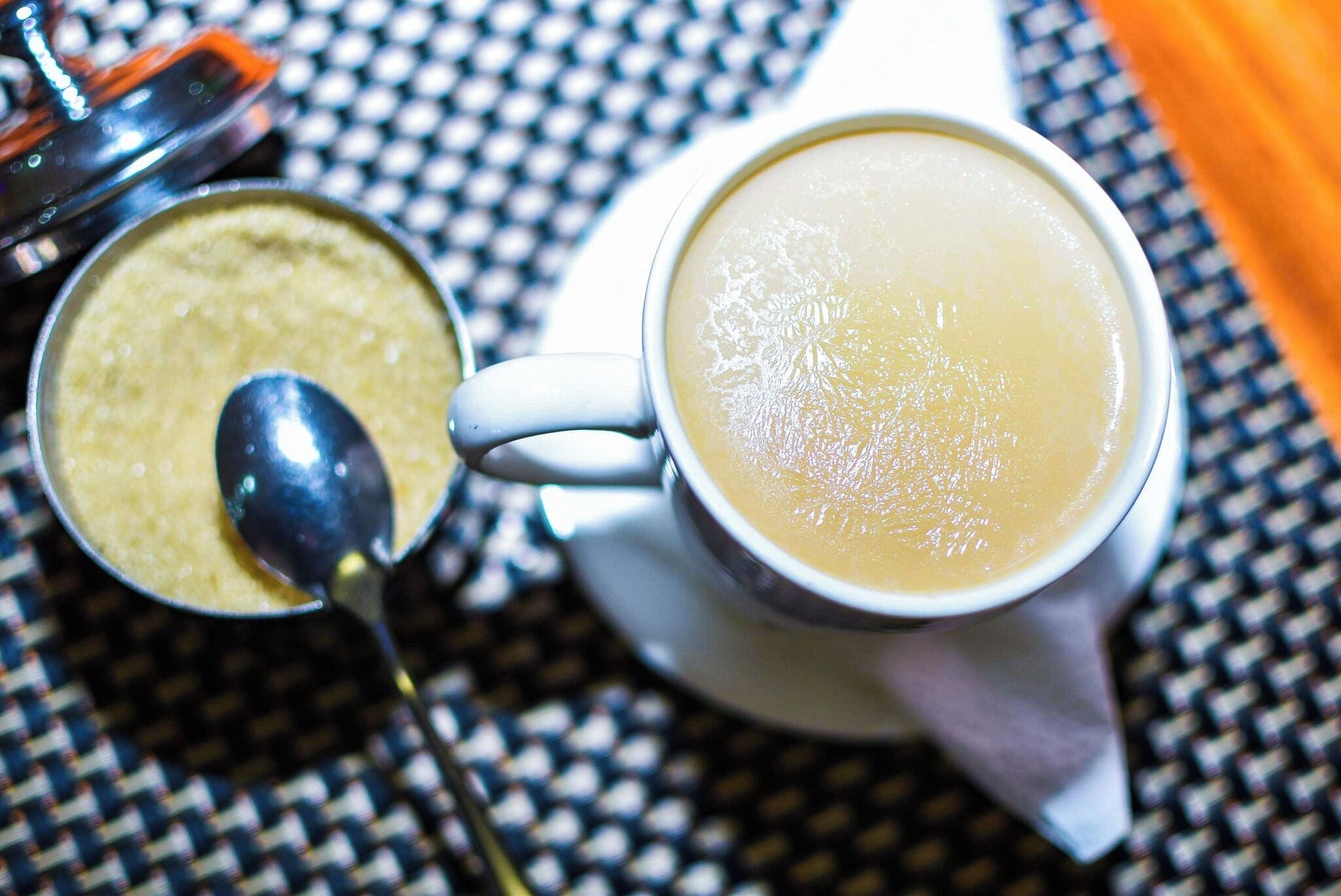 A cup of coffee with a spoon and a container of creamer on a checkered tablecloth.