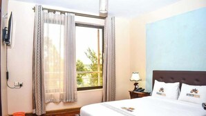 Una habitación de hotel con una cama, una mesita de noche, una lámpara y una ventana con cortinas.