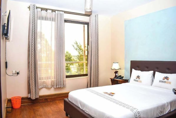 Una habitación de hotel con una cama, una mesita de noche, una lámpara y una ventana con cortinas.