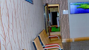 Un área de espera con una fila de sillas, una pantalla de televisión mostrando un paisaje y un muro con diseño.